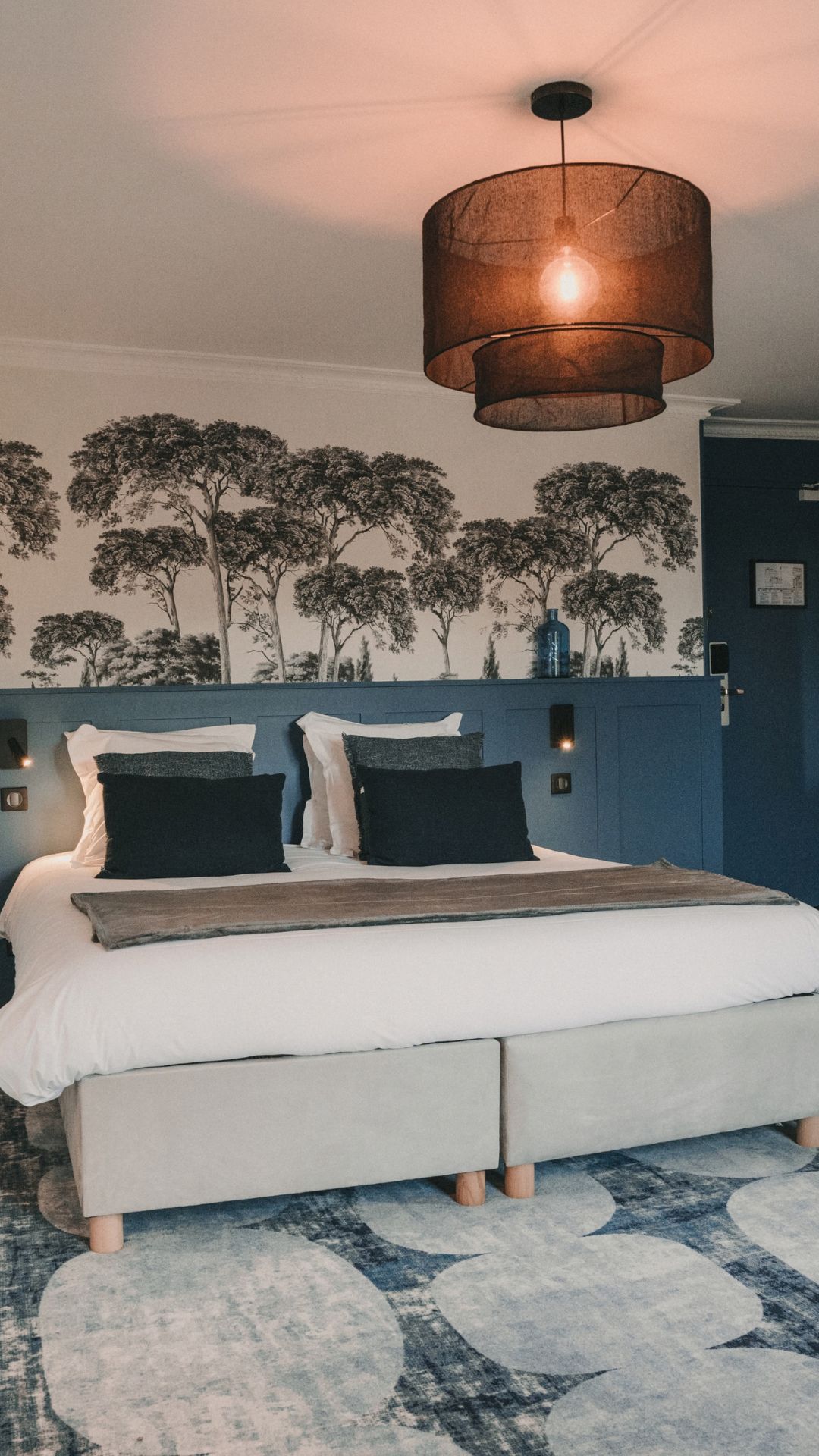 Chambre moderne avec lit, papier peint arbres et suspension noire